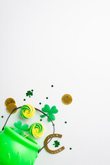 St Patrick's Day concept. Top view vertical photo of green pot with meringue candies gold coins horseshoe clovers and confetti on isolated white background with copyspace