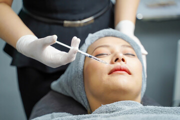 Fototapeta premium Closeup hands of beauty doctor in medical grove holding beauty skin syringe injecting the customer's face. Beauty skin concept