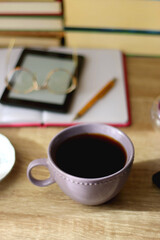 Notebook, pen, tablet, reading glasses, books, phone, candle, bowl of biscuits and cup of tea on the table. Selective focus.