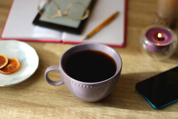 Notebook, pen, tablet, reading glasses, books, phone, candle, bowl of biscuits and cup of tea on the table. Selective focus.