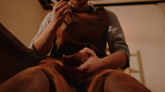 Shoemaker in workshop making handmade shoes. Craftsman's hands stretching leather and nailing it with hammer to shoe last in shoe products tailoring studio.