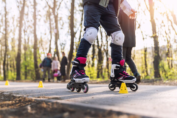 Group of little children enjoy having fun learning inline roller skate slalom with plastic cones on road in city park outdoors on sunny spring day. Healthy kid outside sport exercise activities