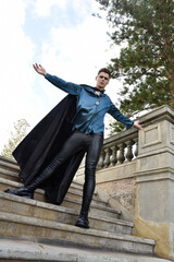 Fototapeta na wymiar portrait of handsome brunette male model wearing fantasy medieval prince costume, romantic silk shirt. Wandering around historical castle location background with stone staircase.