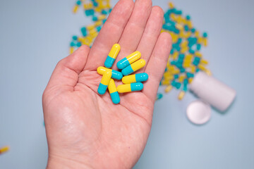 Multiple colors pills in hand on blue background. Taking Your Medication. Medicine concept.