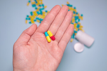Multiple colors pills in hand on blue background. Taking Your Medication. Medicine concept.
