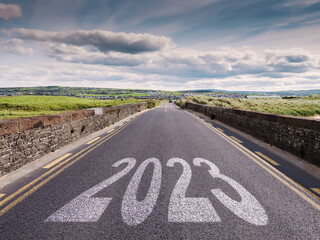 Small narrow high quality asphalt road with stone fences on each side and big sign 2023. Blue cloudy sky and green fields. Warm sunny day. West of Ireland. Travel concept.