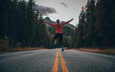 Young girl jumping, with her back turned, on the famous Icefields Parkway road in the Canadian Rockies