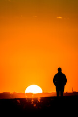 Fototapeta na wymiar Silhouette of a man with a coat and his hands in his pockets, watching the sunset