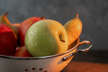 Colander with washed fruits on a wooden table, sunlight through the window. Closeup