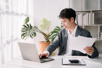 Asian business man working at office with laptop and documents on his desk, financial adviser analyzing data.