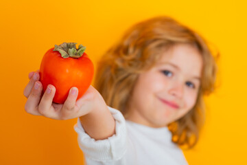 Fototapeta na wymiar Kid with persimmon in studio. Studio portrait of cute child hold persimmon isolated on yellow background.