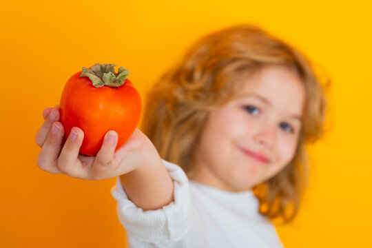 Kid With Persimmon In Studio. Studio Portrait Of Cute Child Hold Persimmon Isolated On Yellow Background.