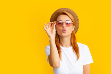 Redhead girl sends an air kiss. Portrait of young beautiful woman in straw hat and sunglasses. Summer mood. Young smiling cheerful caucasian pretty gild ginger hair wearing summer hat and glasses.