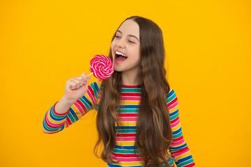 Teen girl hold lollipop caramel on yellow background, candy shop. Teenager with sweets suckers. Excited face, cheerful emotions of teenager girl.