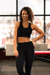 Fototapeta na wymiar Slim athletic African American woman in sportswear doing exercises with dumbbells on a bench press in the gym, copyspace.