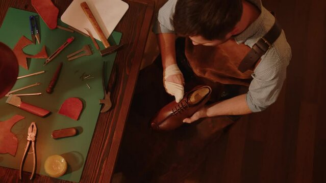 Shoemaker in workshop rubs leather shoe top view. Manufacture and tailoring of handmade shoes.