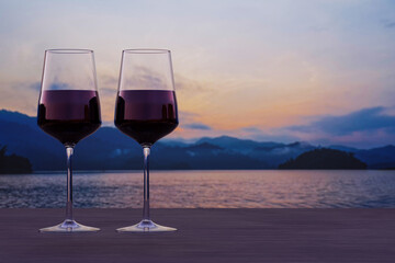 Two glasses of red wine with view of sunset over lake and mountains.