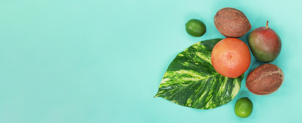 Tropical fruits, top view on a blue background. Grapefruit, coconuts, limes and mangoes, tropical leaf on a stretched background