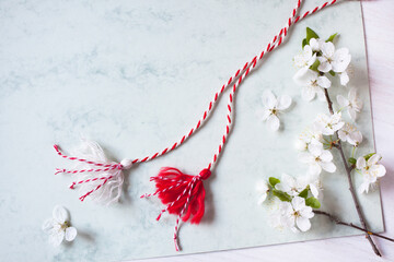 Flowering branches of cherry plum, red-white martenitsa cord with tassels on a paper, white wooden...