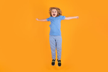Fototapeta na wymiar Full length of excited kid jumping. Energetic kid boy jumping and raising hands up on isolated studio background. Full length body size photo of jumping high child boy, hurrying up running fast.