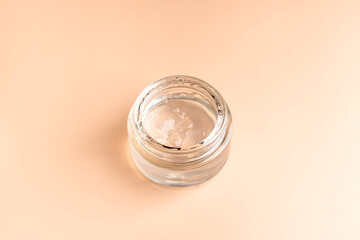 Jar with transparent cosmetic product, gel or cream on beige pastel background. Unbranded package with an antioxidant cream for selfcare. View from above.