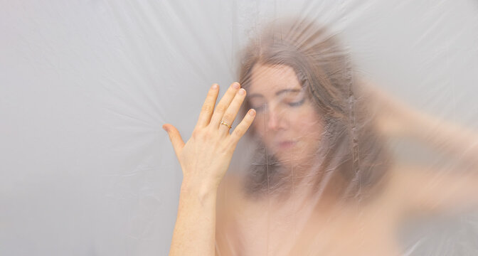 blurred, fuzzy image of sensual romantic young naked red hair woman portrait behind plastic film, shows hand with wedding ring, looks like renaissance madonna, looking down