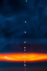 The drop falls into a thick liquid with a blue-yellow background in the smoke. Abstract colorful background.