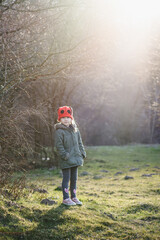 Caucasian little girl in walks in the park in the rays of the setting sun. A child in a red hat...