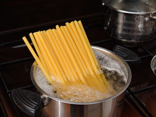 Thick large pasta is cooked in an iron pot with boiling water. On a dark background