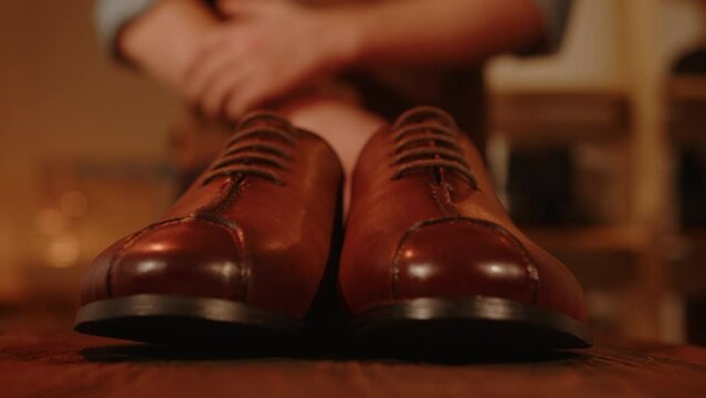 Shoemaker puts male shoes on table in workshop. Craftsman demonstrating handmade shoes. Success and pride in result of work.