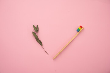 Eco-friendly bamboo toothbrush, dental cleaner and a green leaf on a pink background.