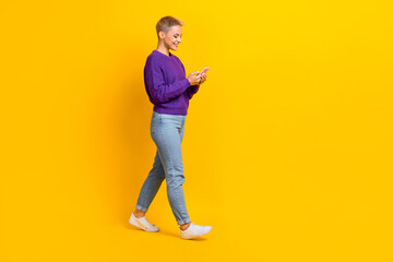 Fototapeta premium Full length profile portrait of nice positive person hold telephone walking isolated on yellow color background