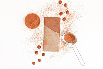 Chocolate bar in an open package, nuts, cocoa, strainer on a white background