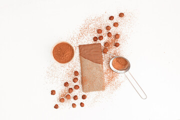 Chocolate bar in an open package , nuts, cocoa, strainer on a white background, top view
