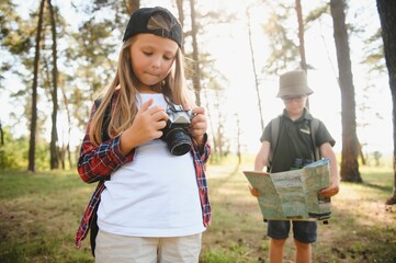 Group of curious happy school kids in casual clothes with backpacks exploring nature and forest together on sunny autumn day.