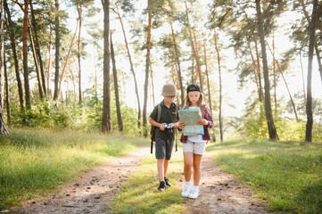 Happy excited school children with backpacks in casual clothes enjoying walk in forest on sunny autumn day, two active kids boy and girl running and playing together during camping trip in nature.