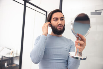 Focused transgender person examining his appearance after the makeup application