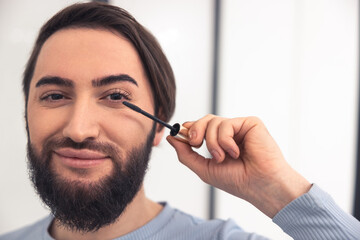 Pleased transgender person using the eye cosmetics