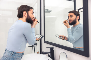 Serious concentrated young man using eye cosmetics