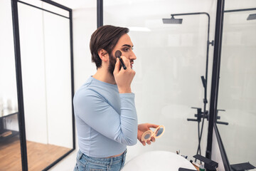 Focused young man standing in the bathroom during makeup application