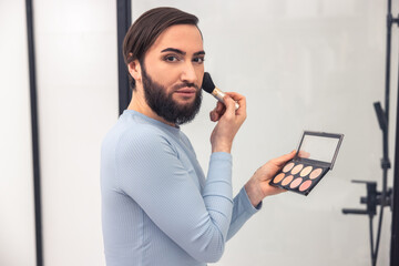 Serious man looking at the mirror during the blush application