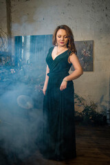 portrait of a beautiful brunette smiling woman  in vintage room with flowers and smoke in dark green long dress