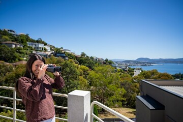 Girl using binoculars on a balcony in a city next to the sea, seaside town