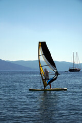A man on a windsurf in the bay with a yacht in the background. Man learning to windsurf in the bay. Windsurfing in Turkey.