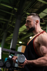 Fototapeta na wymiar A brutal muscular man with a beard and a ponytail does a biceps exercise in the gym