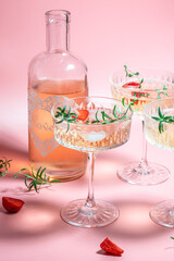 refreshing fruit cocktail or punch with wine champagne, strawberries, ice and rosemary on pink background. Freeze motion splash drops of cocktail