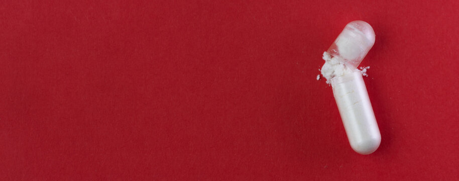 Close up view of single probiotic capsule with white powder on red background.