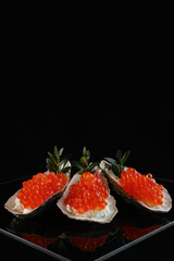 Red caviar in oyster flaps. A useful omega. An exquisite snack. Black background. A festive snack. Copy space.Vertical photo.