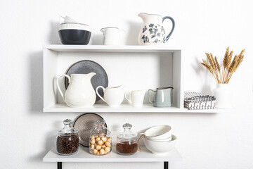 beautiful white shelves with kitchen utensils on a white textured wall. kitchen interior in white tones. front view. ecologically clean kitchen.