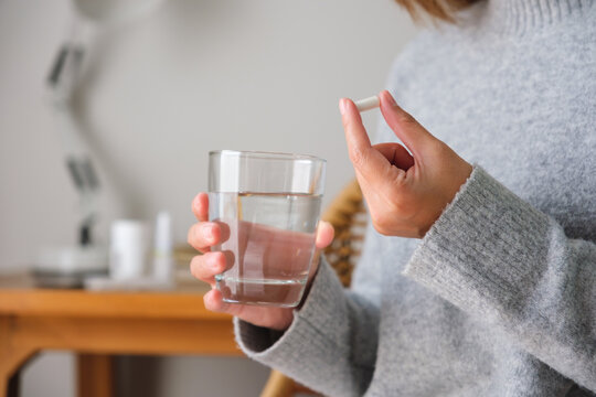 Closeup image of a woman holding white pills and a glass of water